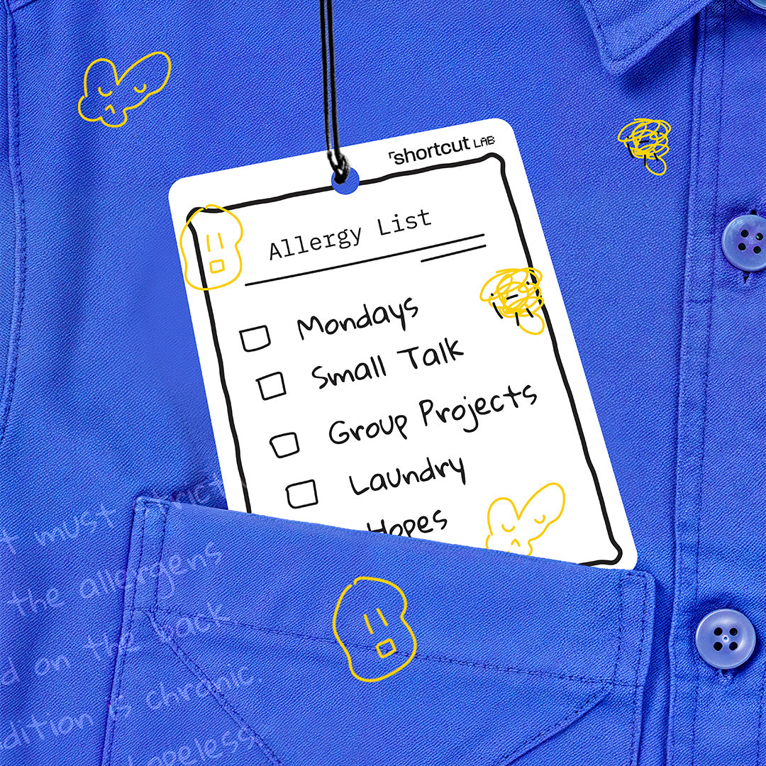 Shortcut Lab ‘Allergy List’ car fragrance card in Amber Orchard scent featuring humorous checklist design, styled on a blue shirt background with yellow doodles.